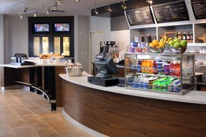 A modern coffee shop counter with a coffee machine, a beverage dispenser, and a fruit display. - Courtyard by Marriott Houston Pearland (Pearland)