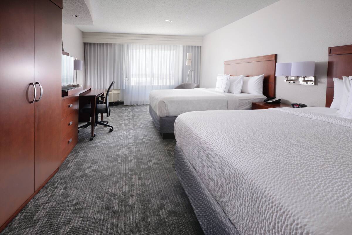 A hotel room with two beds, a desk, and a chair.
