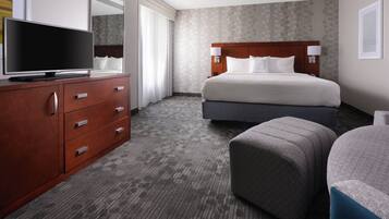 Una habitación de hotel con una cama grande, un televisor sobre una cómoda de madera y una alfombra gris.
