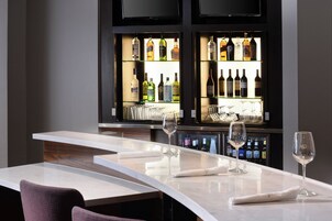 Una zona de bar con una barra de mármol curvada, copas de vino y una variedad de botellas en estantes.