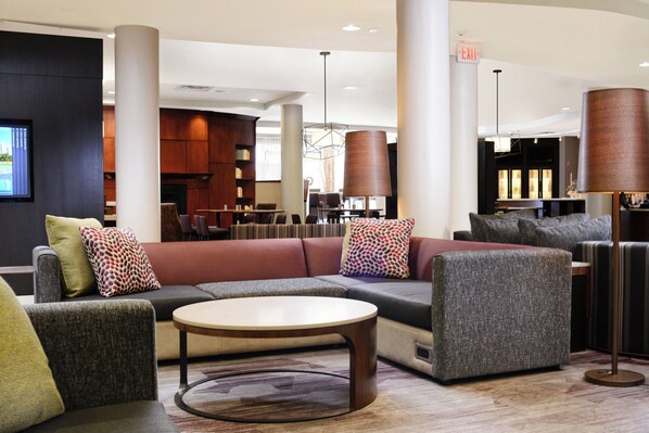A modern lobby with a sectional sofa, armchairs, a coffee table, and a large floor lamp. - Courtyard by Marriott Houston Pearland (Pearland)