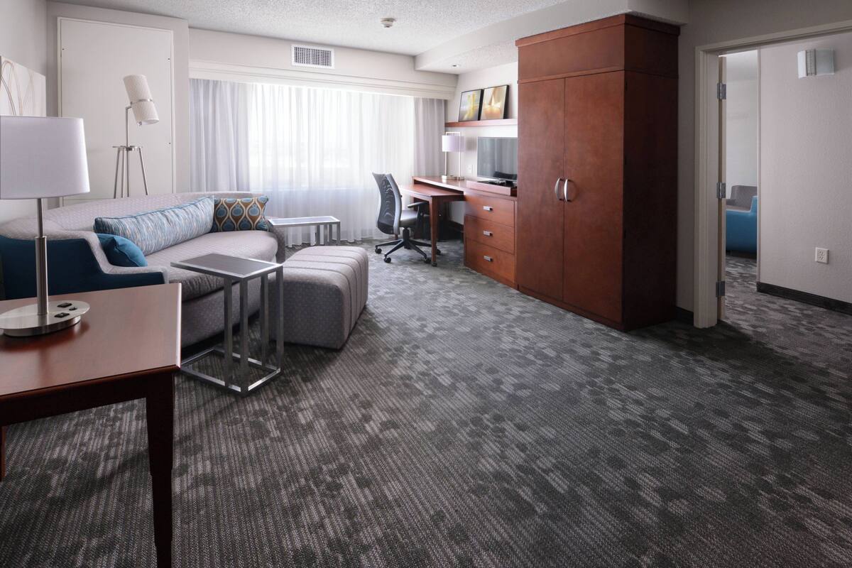 A hotel room with a sofa, ottoman, desk, and wardrobe.