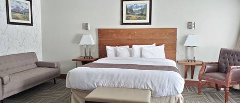 A hotel room with a large bed, a wooden headboard, a sofa, a chair, and two bedside tables with lamps.