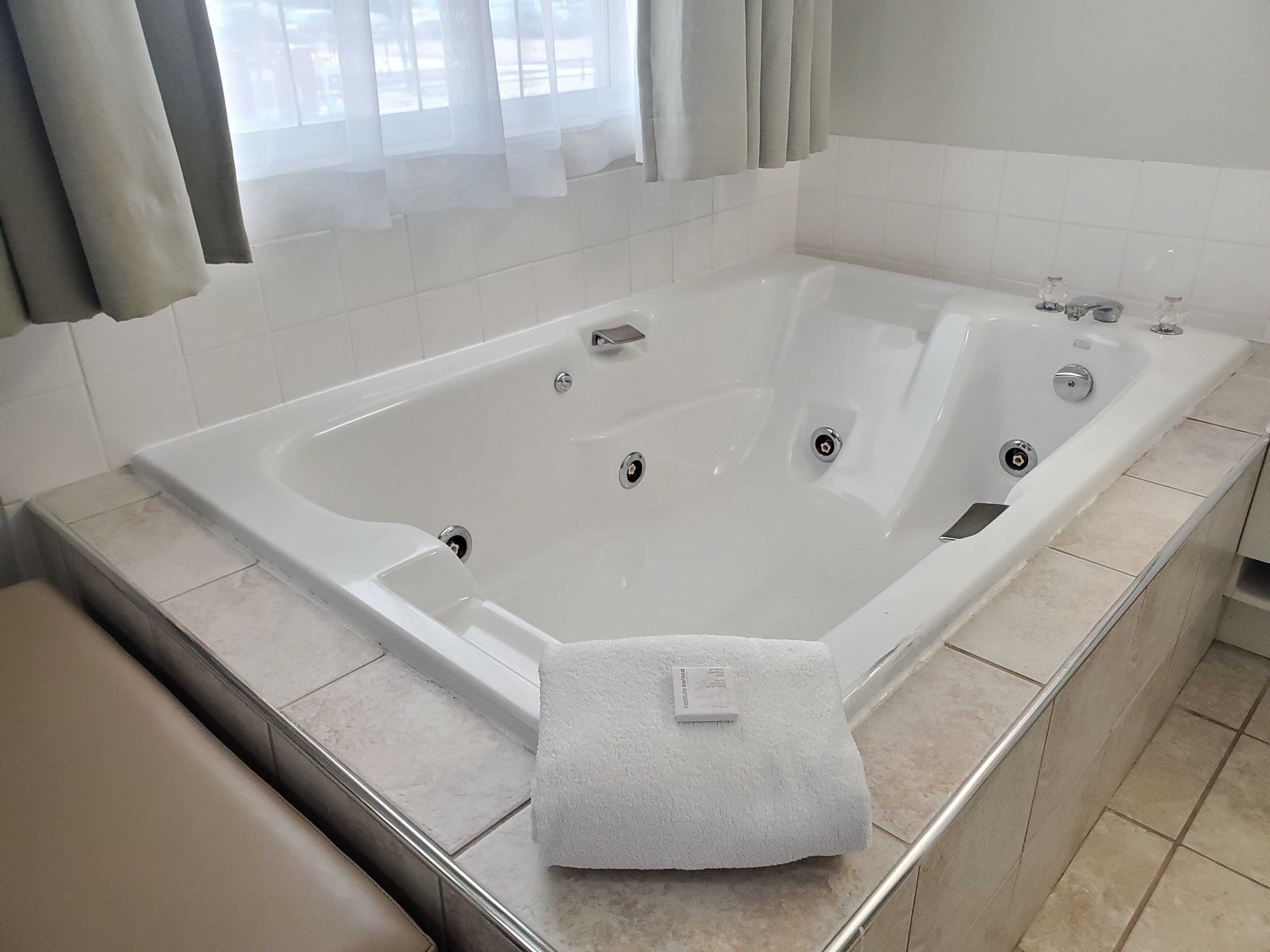 Eine große, rechteckige Badewanne mit mehreren Wasserhähnen und einem Handtuch am Rand.