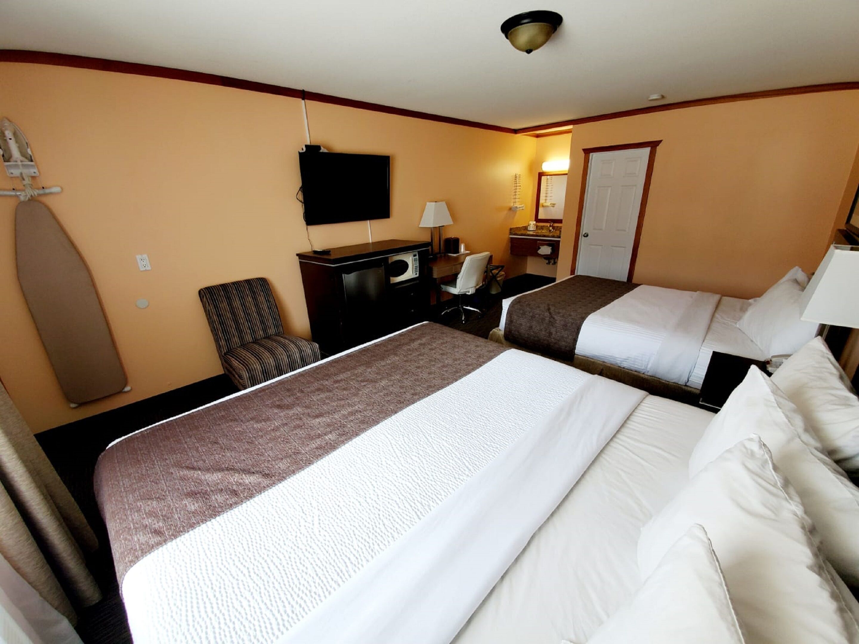 A hotel room with two beds, a desk, a chair, a television, and a door.