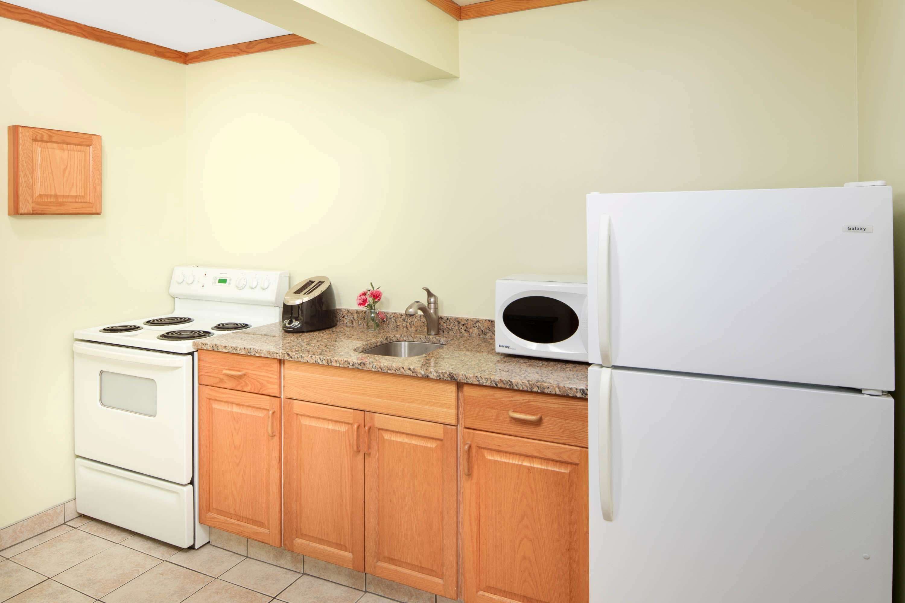 A kitchen with wooden cabinets, a white stove, a microwave, and a refrigerator.
