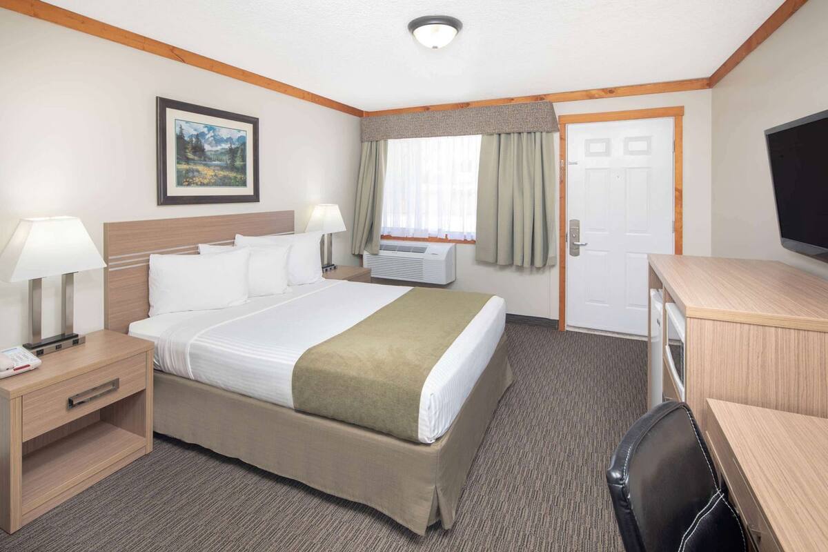 A hotel room with a bed, bedside lamps, a television, a desk, and a window with curtains.
