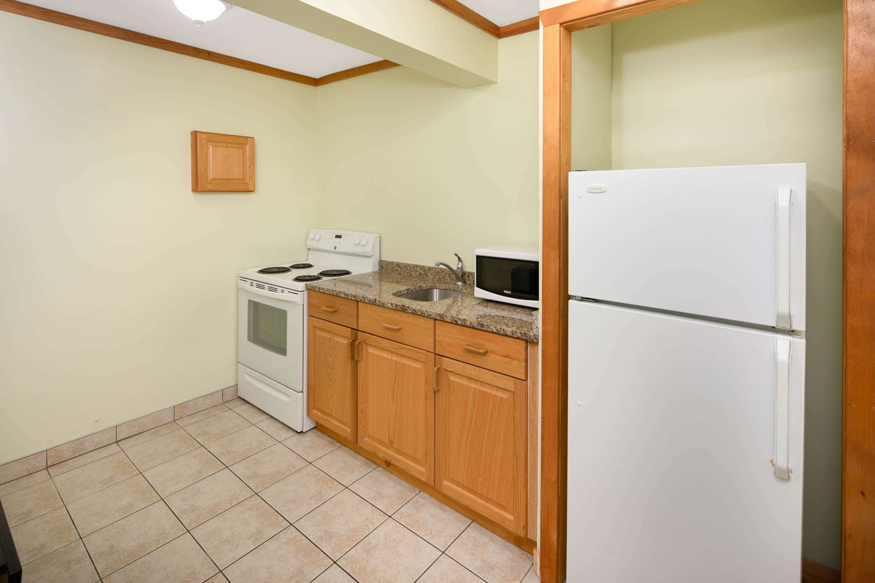 Una cocina con armarios de madera, estufa, microondas y refrigerador.