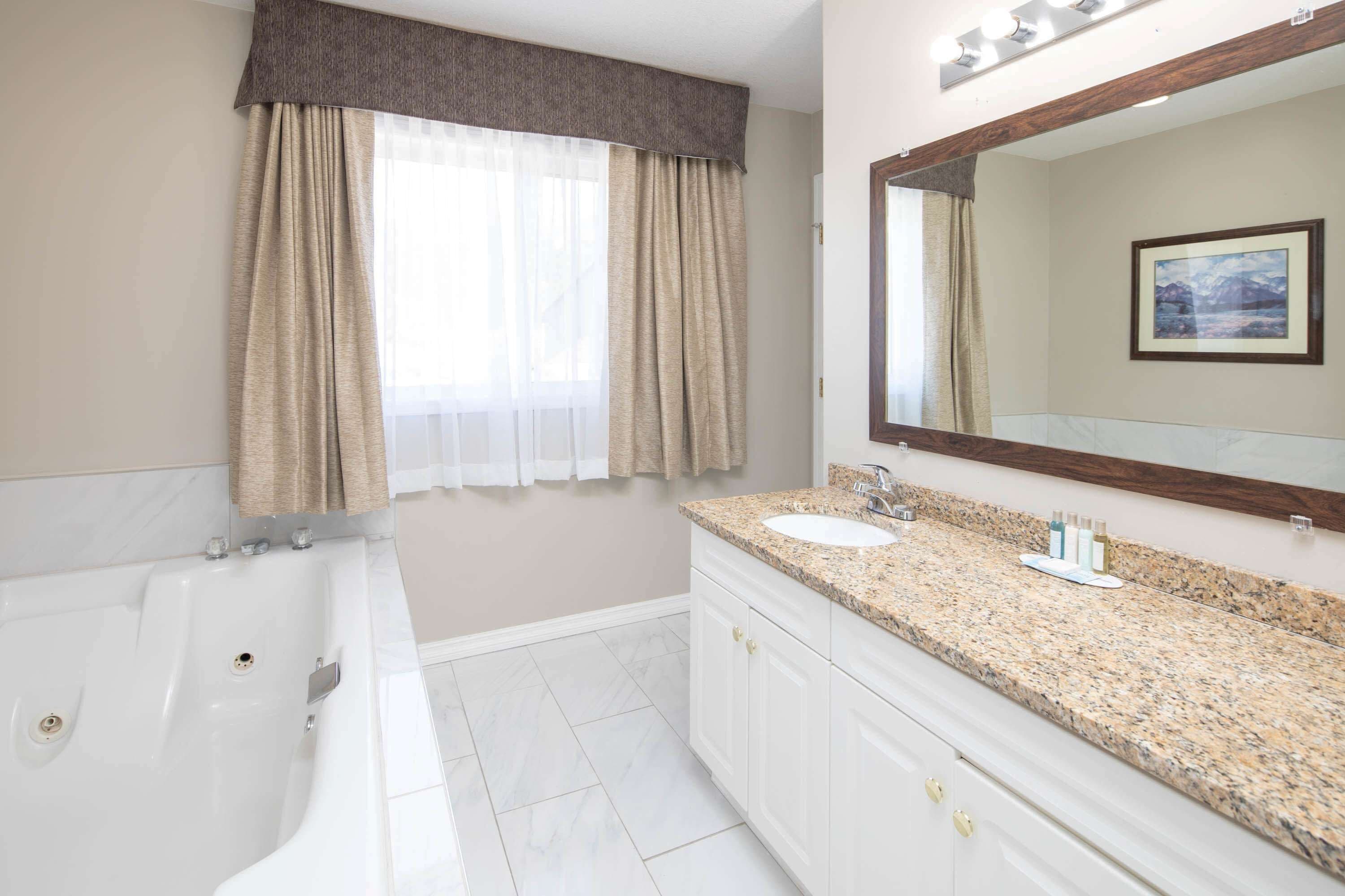 A bathroom with a bathtub, sink, vanity, and a large mirror.