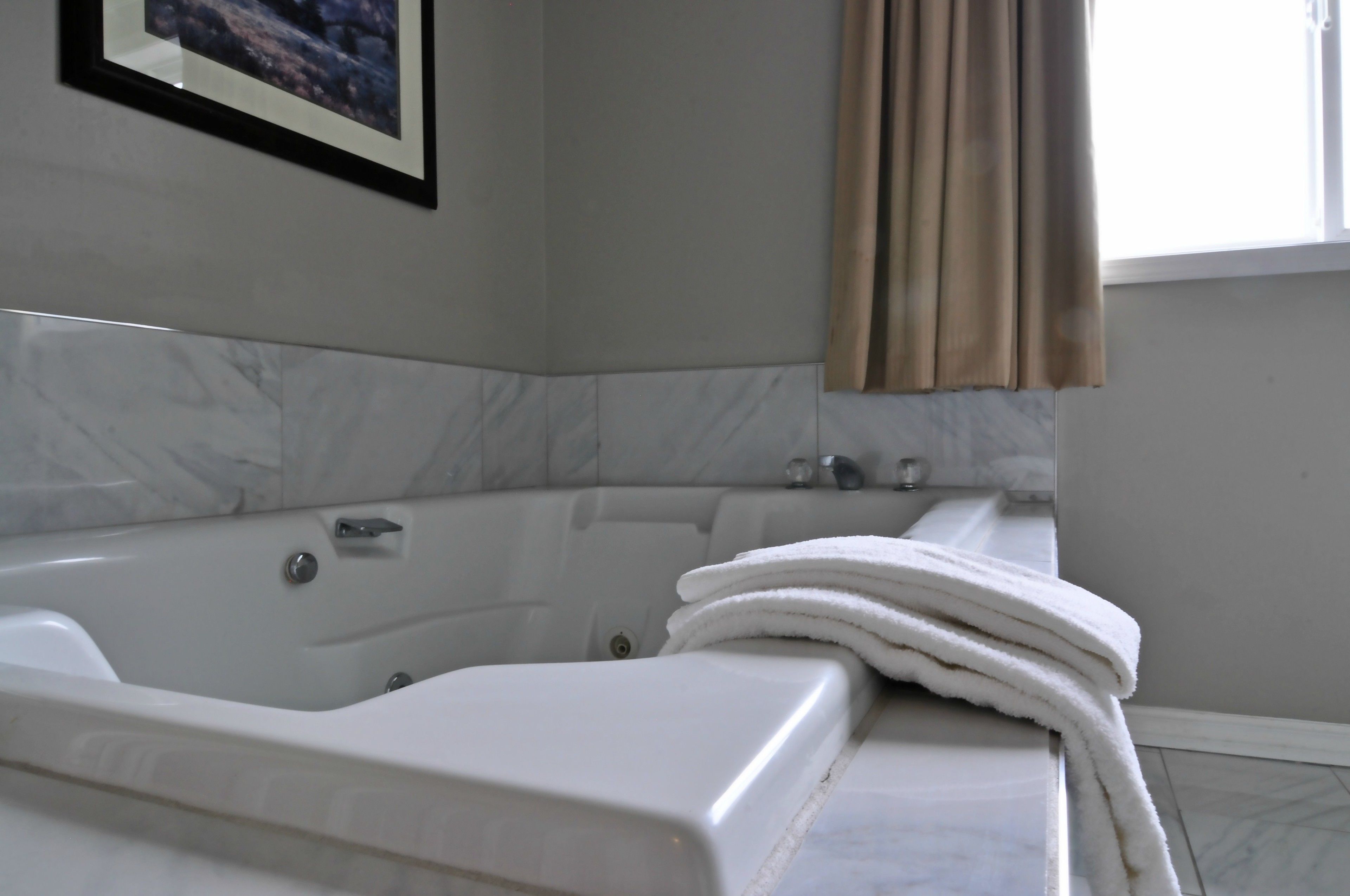 A modern bathroom with a large bathtub, a framed picture on the wall, and a window with curtains.