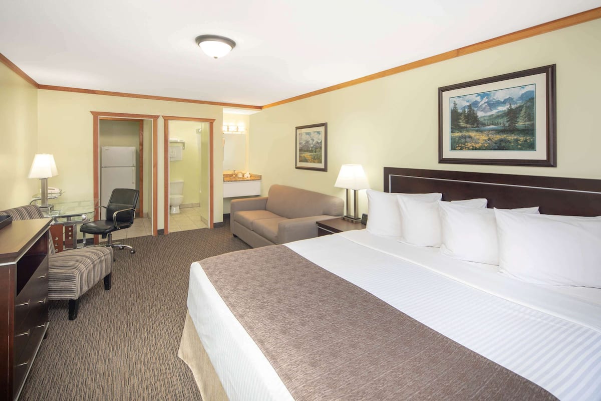 A hotel room with a large bed, a desk with a chair, a sofa, and a small table with a lamp.