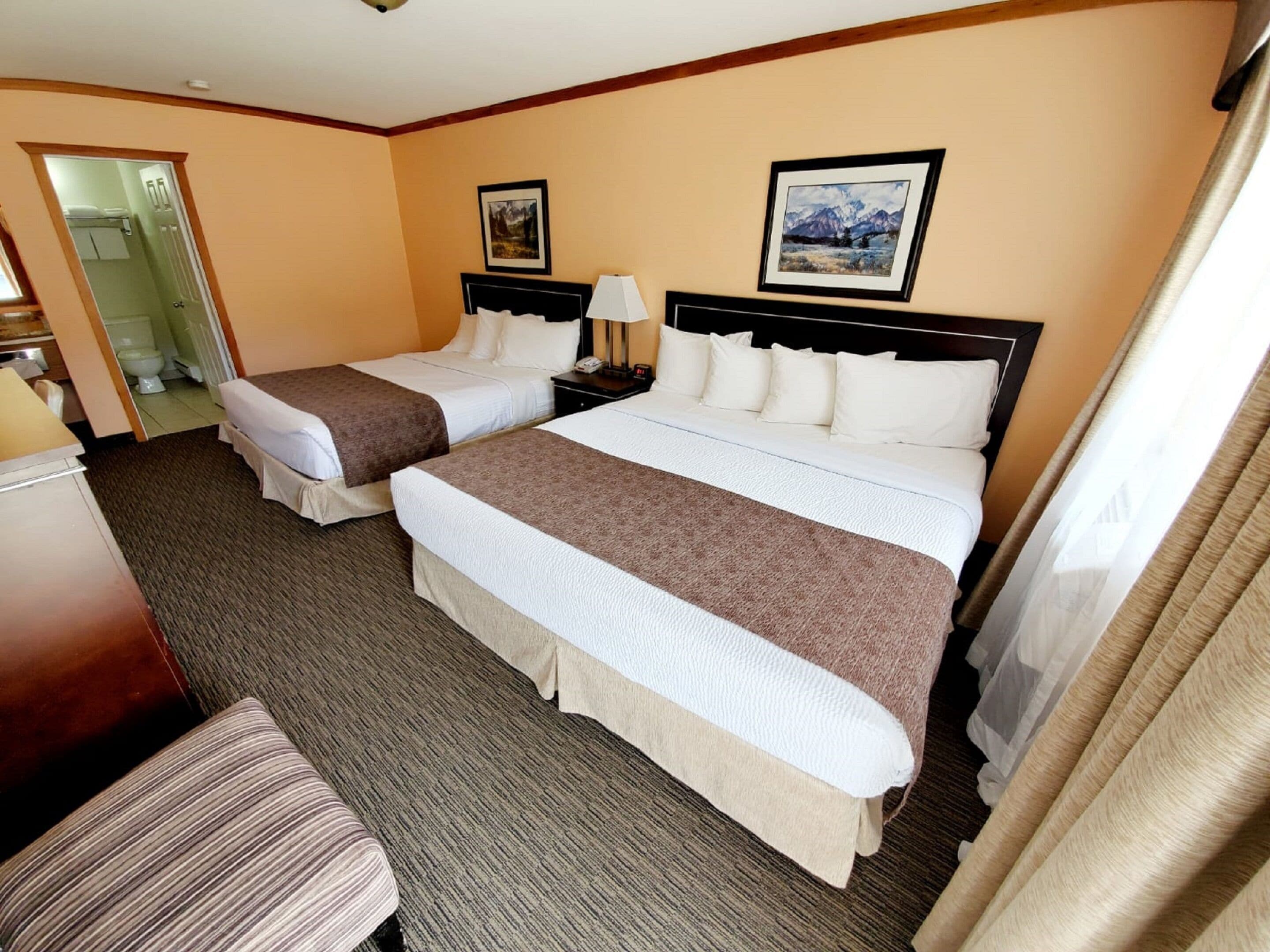 A hotel room with two beds, a desk, and a chair. There are two framed pictures on the wall.