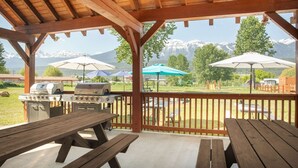 A covered outdoor patio with picnic tables and barbecue grills, overlooking a mountainous landscape. - Travelodge by Wyndham Golden Sportsman Lodge (Golden)