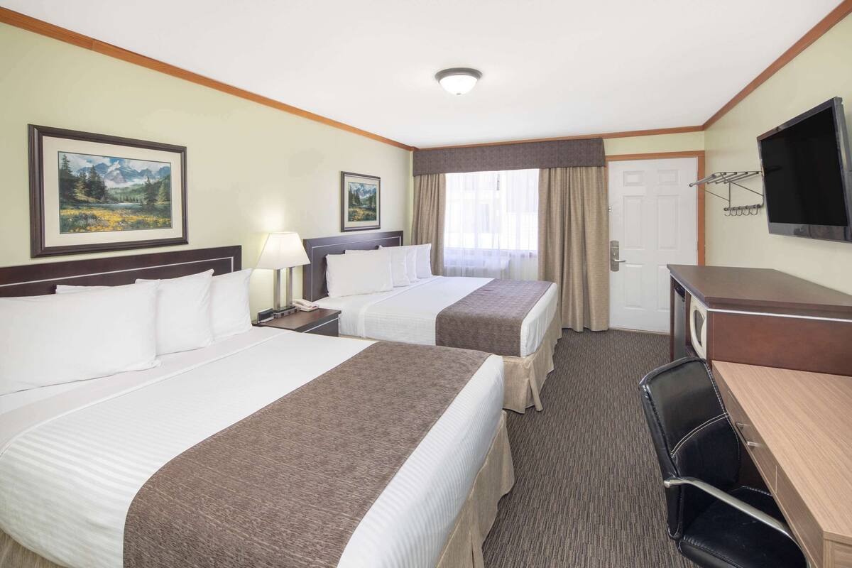 A hotel room with two beds, a desk, a chair, a TV, and a door.