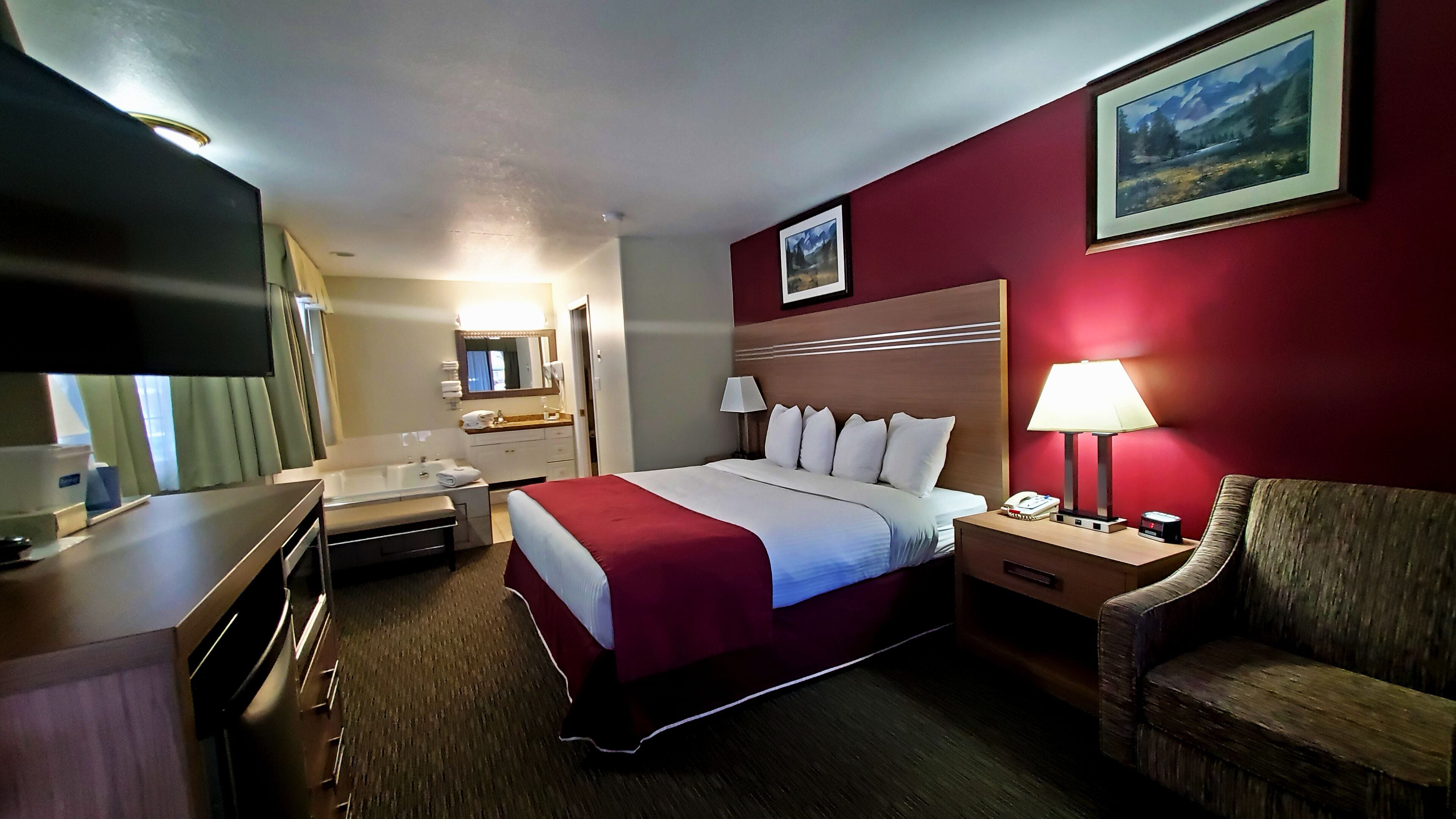 Una habitación de hotel con cama, mesita de noche, lámpara, silla y televisor en la pared.