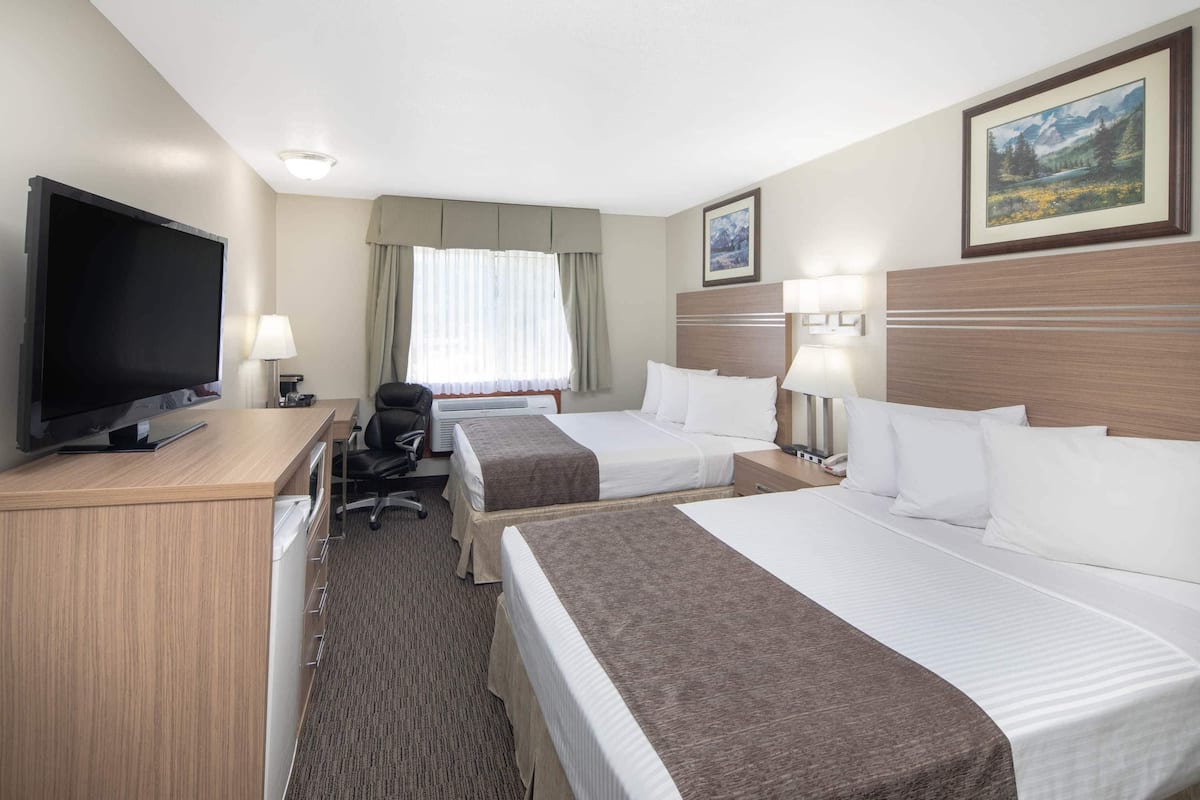 A hotel room with two beds, a desk with a TV, a chair, and a window with curtains.