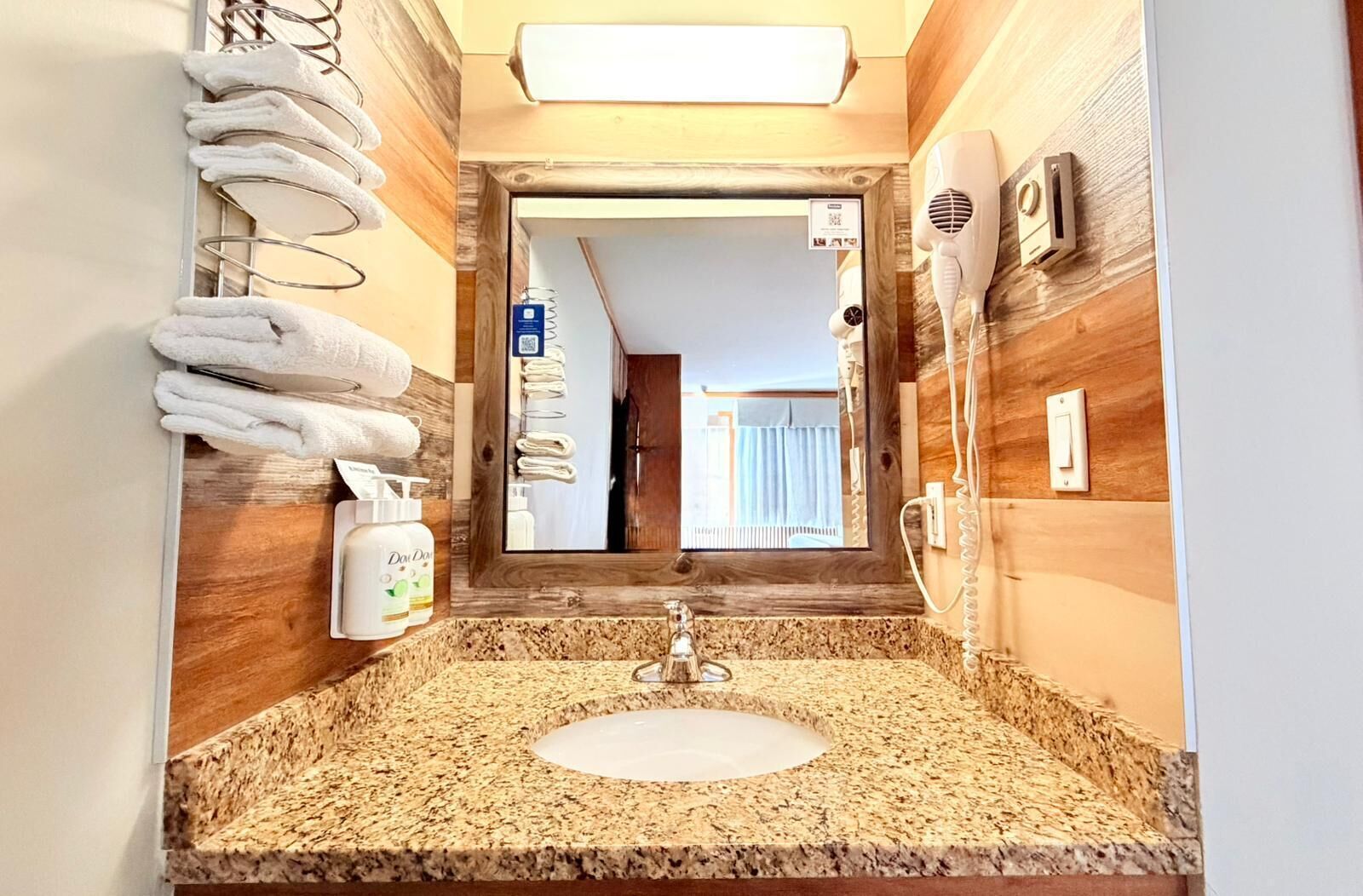 A bathroom with a granite countertop sink, a mirror, a towel rack, a hairdryer, and a bottle of lotion.