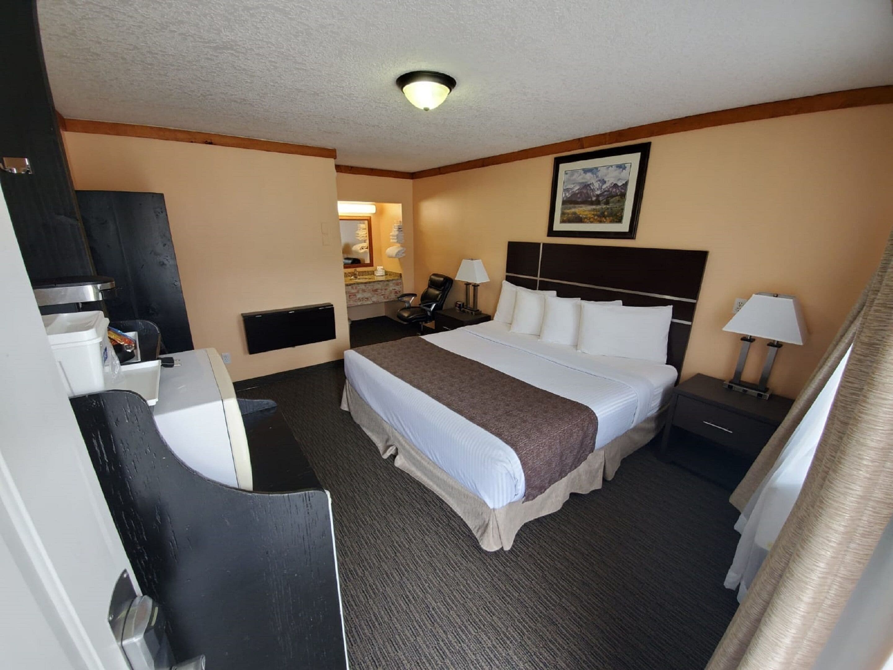 A hotel room with a bed, a desk, a chair, a nightstand, a lamp, and a painting on the wall.