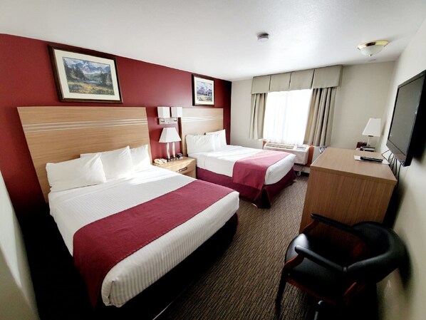 A hotel room with two beds, a desk, a chair, and a TV.