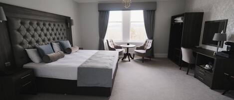 Une chambre d’hôtel avec un grand lit, un bureau, une chaise, une petite table et une grande fenêtre avec des rideaux.