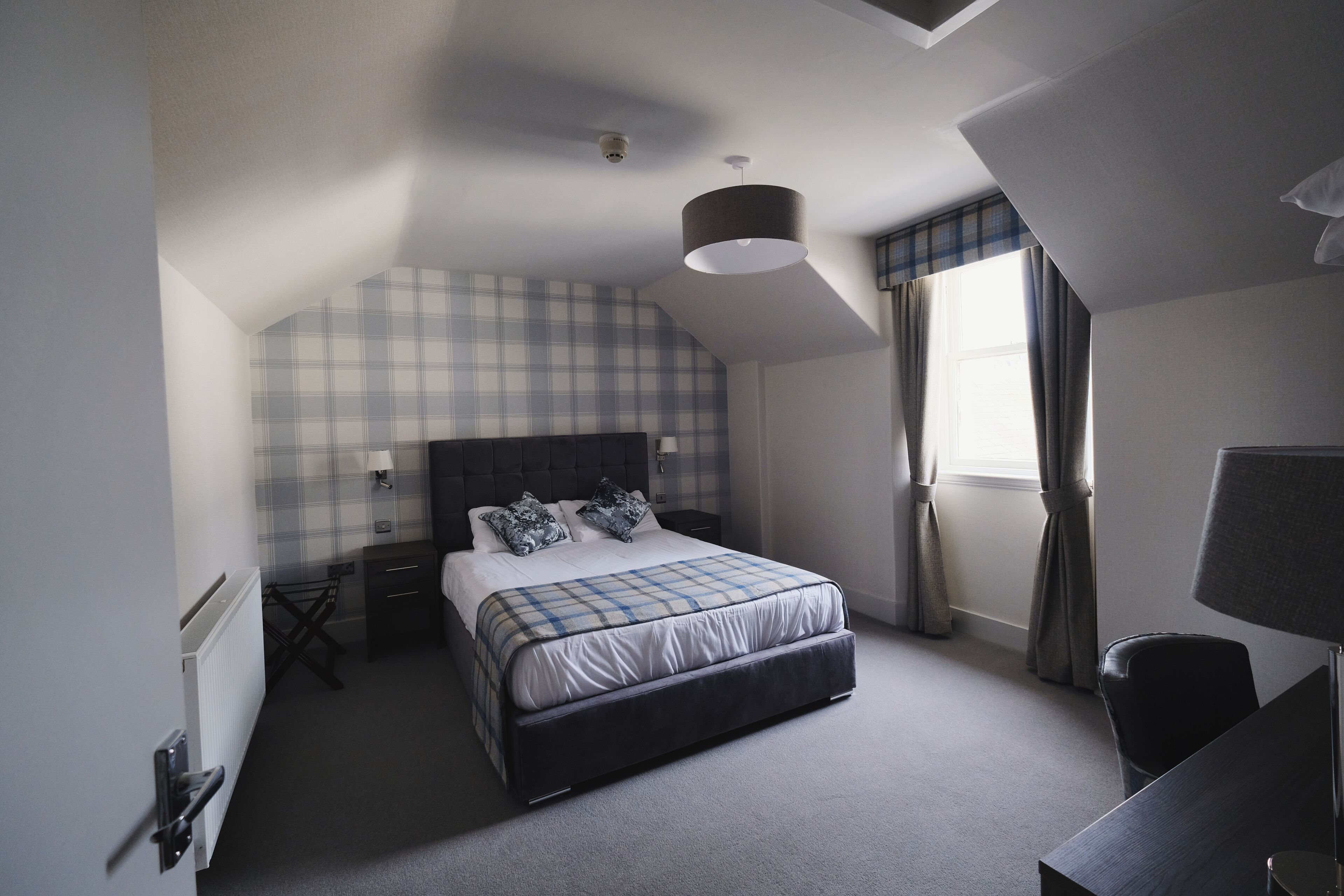 Une chambre à coucher comprenant un lit, un bureau, une chaise, une fenêtre avec des rideaux et un luminaire au plafond.