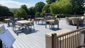 Terraza al aire libre con mesas y sillas, rodeada de árboles.