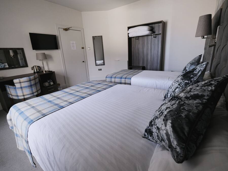 A hotel room with two beds, a television, a mirror, a wardrobe, and a desk with a lamp.