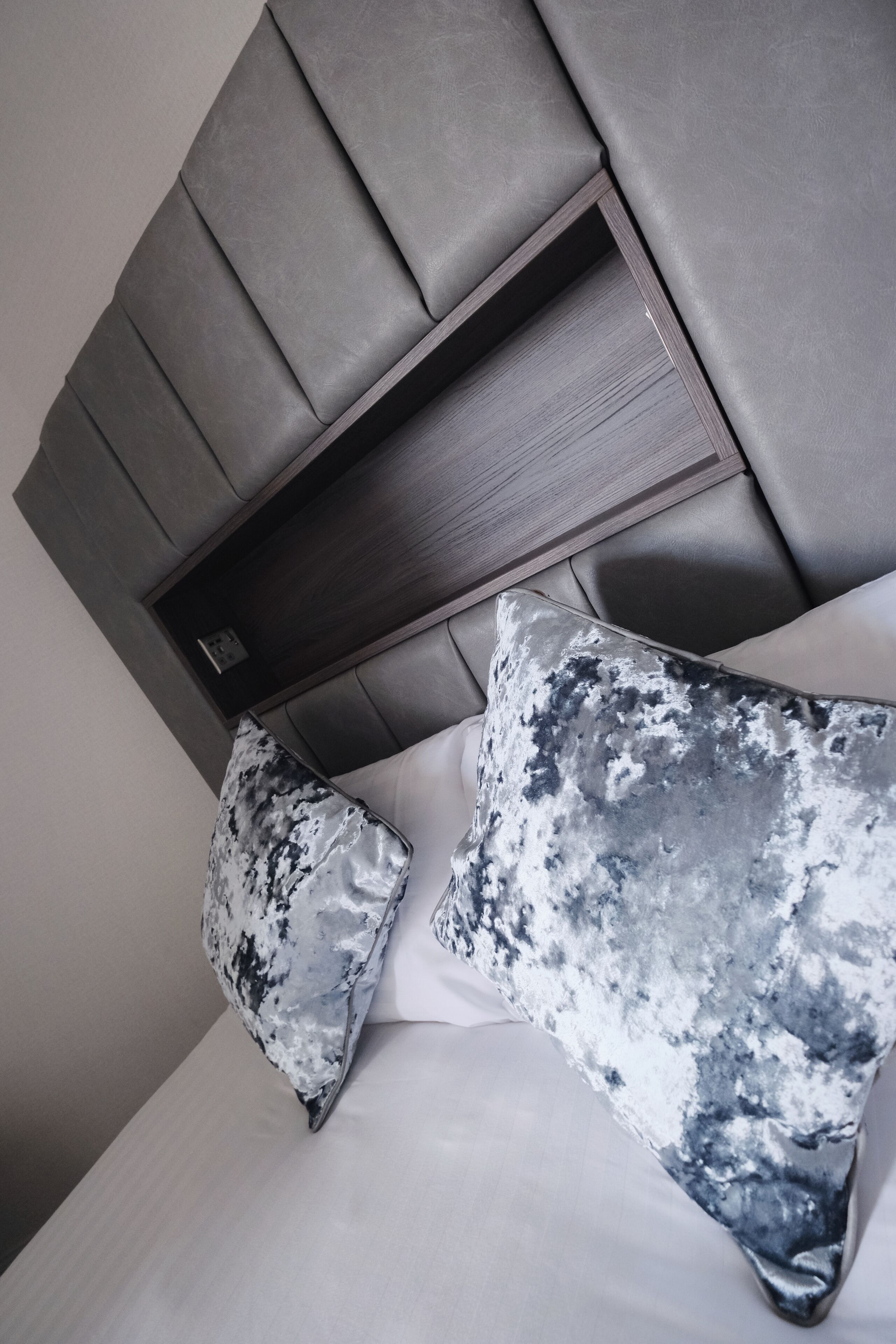 A modern bedroom with a padded headboard, a bed with white linens, and two pillows with a marble-like pattern.