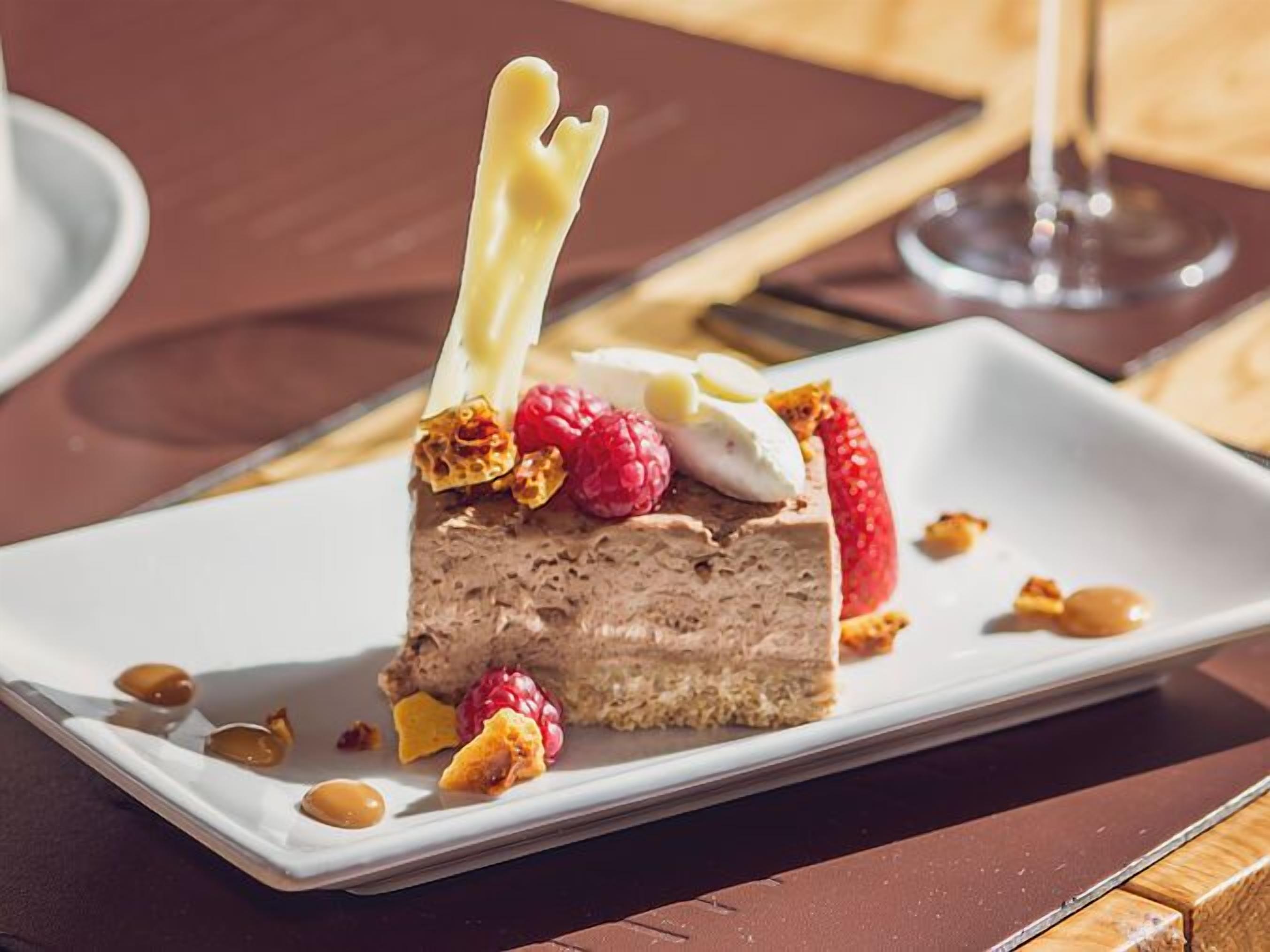 A slice of chocolate mousse cake with raspberries and nuts on a white plate.