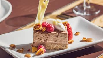 A slice of chocolate mousse cake with raspberries and nuts on a white plate.