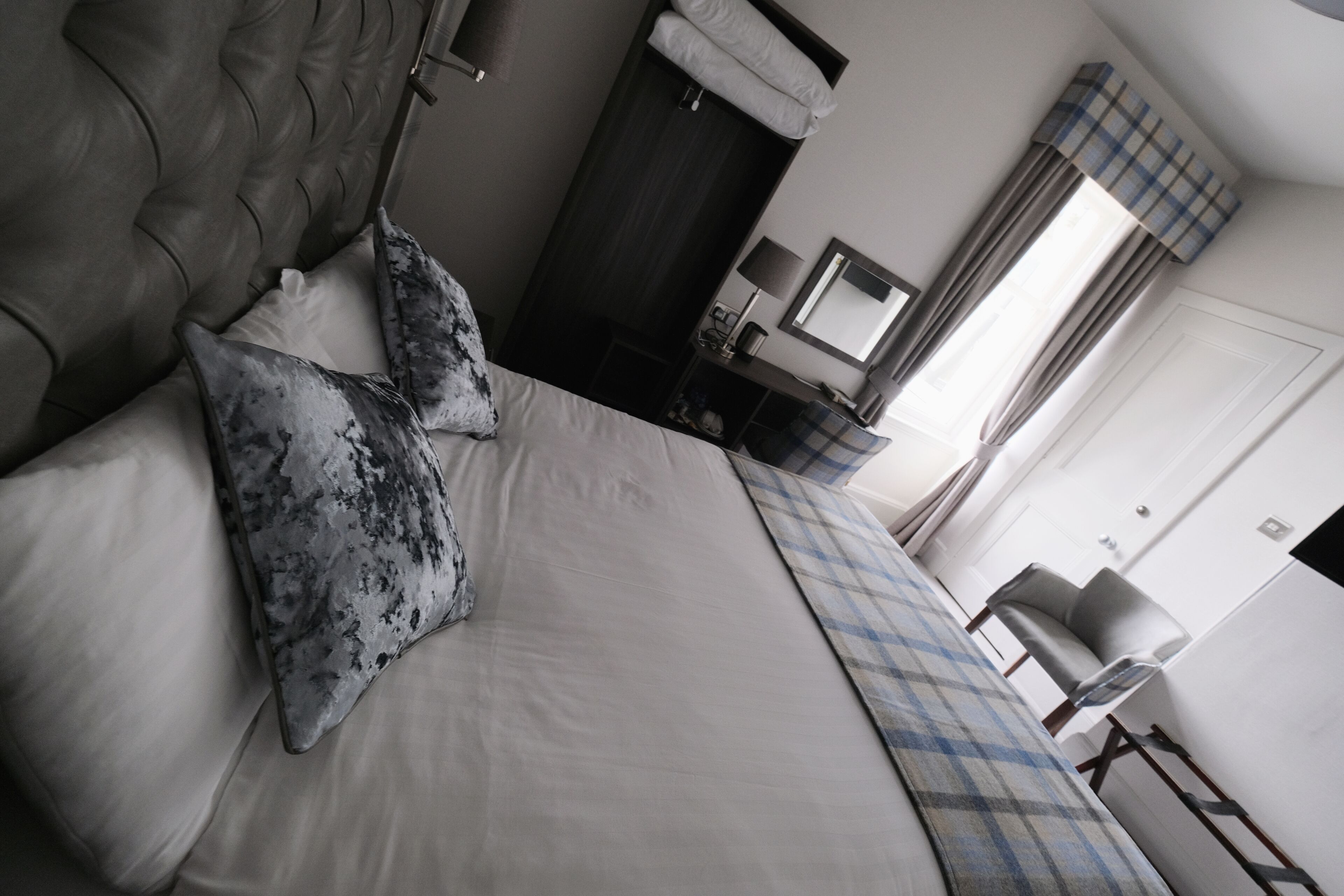 A bedroom with a large bed, a bedside table with a lamp, a wardrobe, and a mirror.