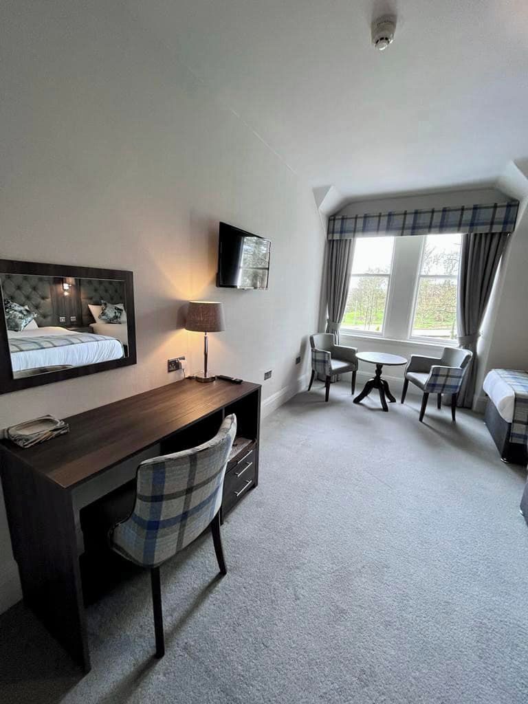 Ein Schlafzimmer mit einem Bett, einem Schreibtisch, einem Stuhl, einem Fernseher und einem Fenster mit Vorhängen.