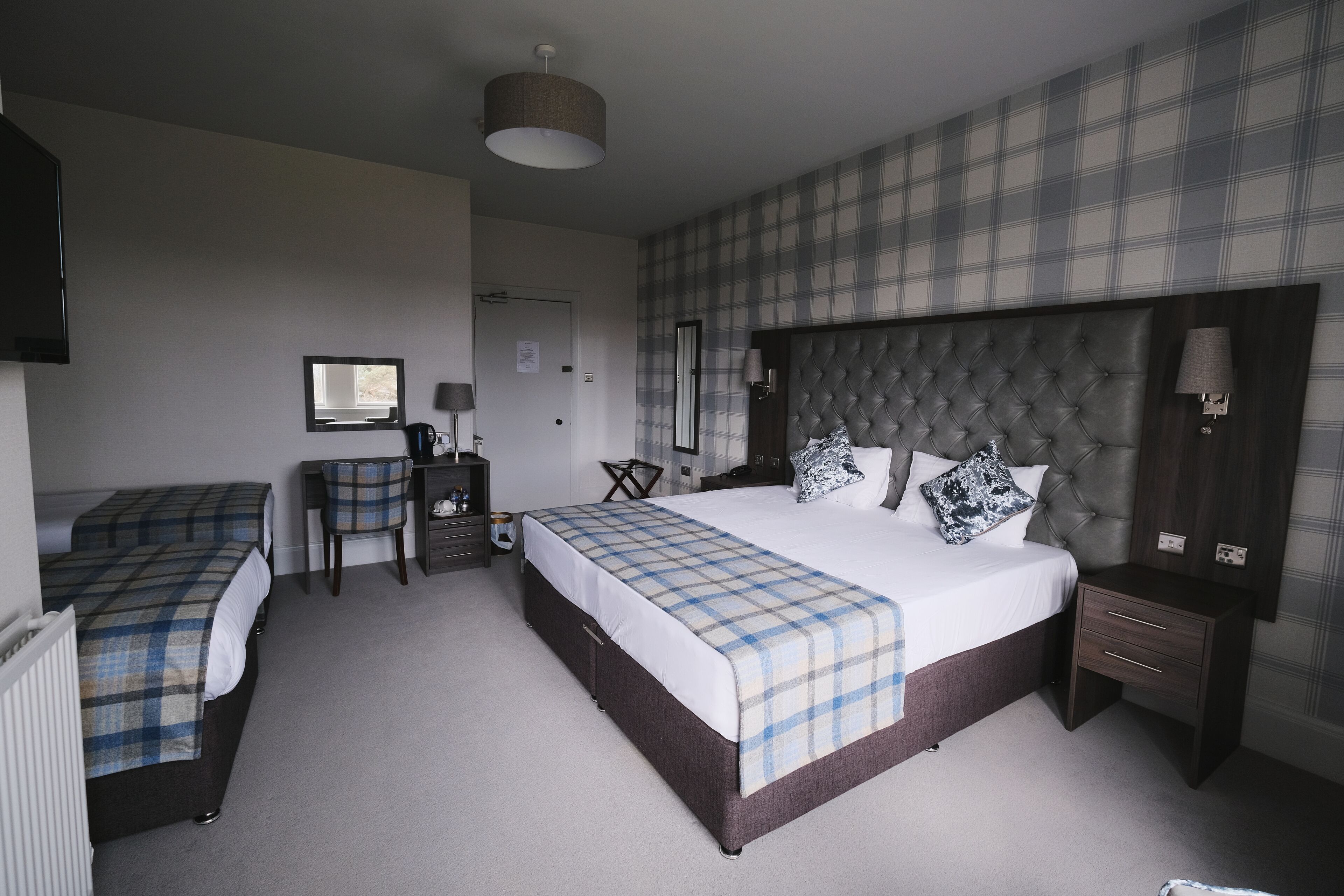 A hotel room with a large bed, a smaller bed, a desk, a chair, and a wardrobe.