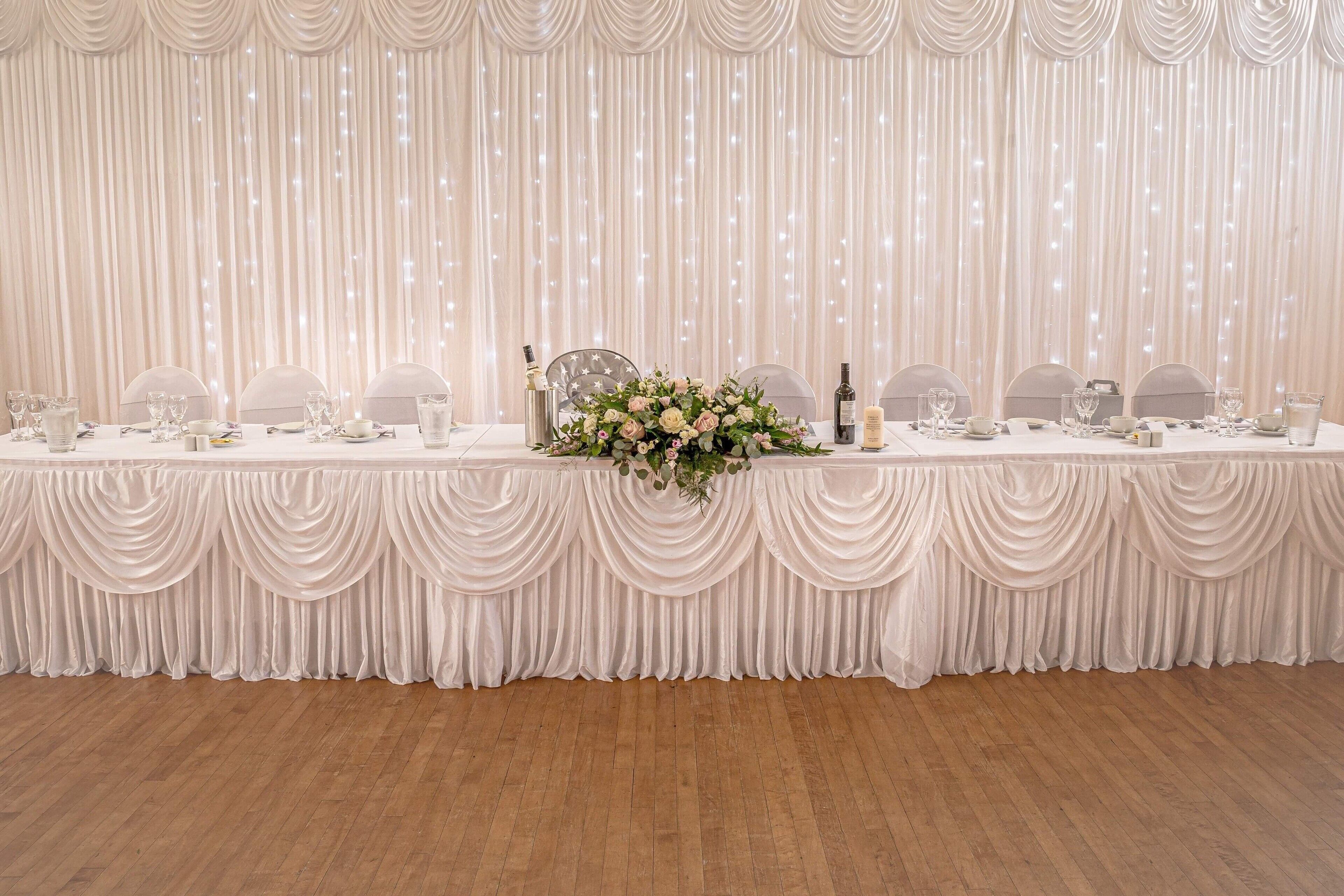 Een lange tafel gedekt met witte tafelkleden, stoelen en een bloemdecoratie.