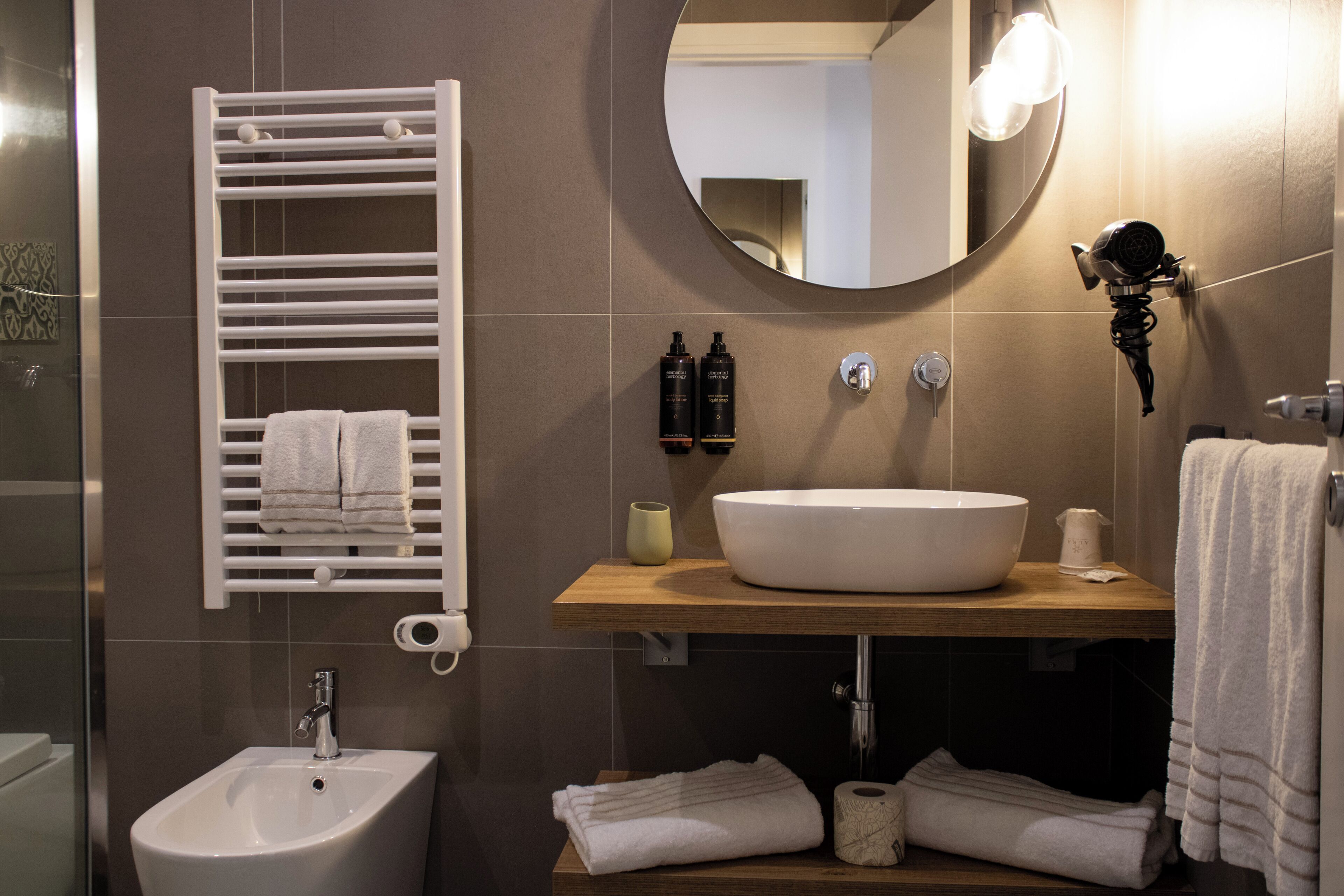 A modern bathroom with a white sink, a towel rack, a mirror, and a bidet.