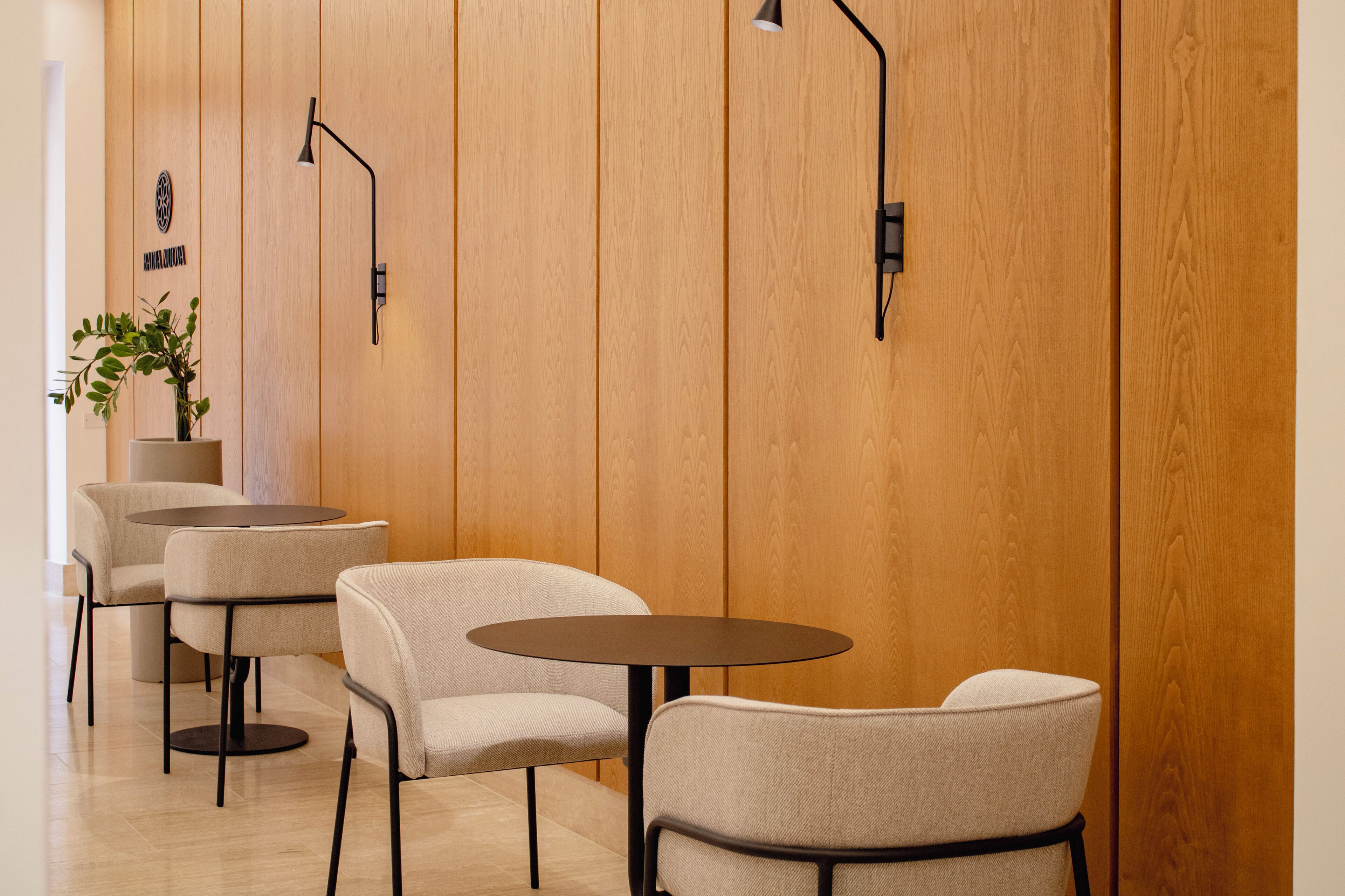 A modern interior with wooden panel walls, a potted plant, and a seating area with round tables and chairs.
