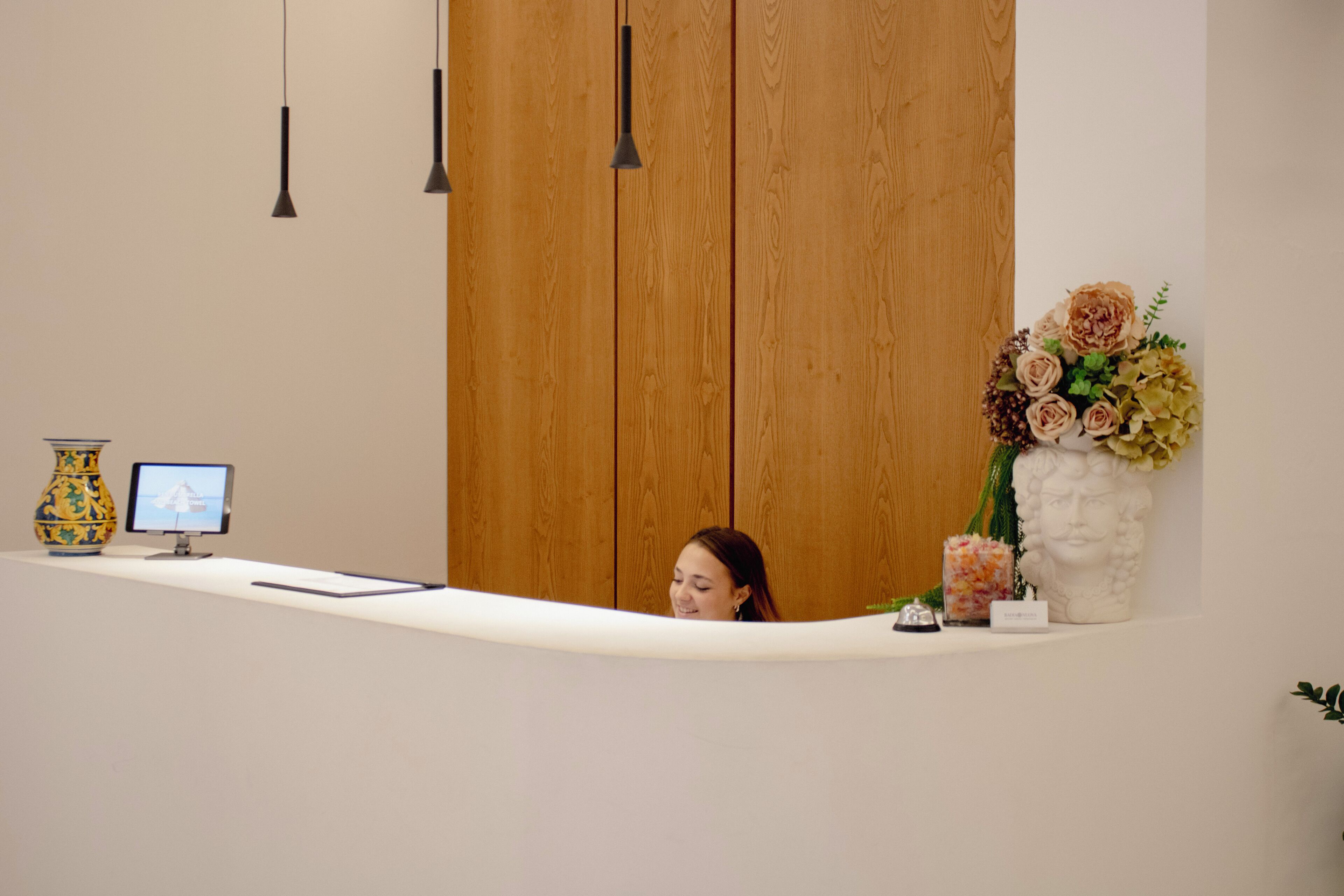 A reception desk with a computer monitor, a vase, and a floral arrangement.