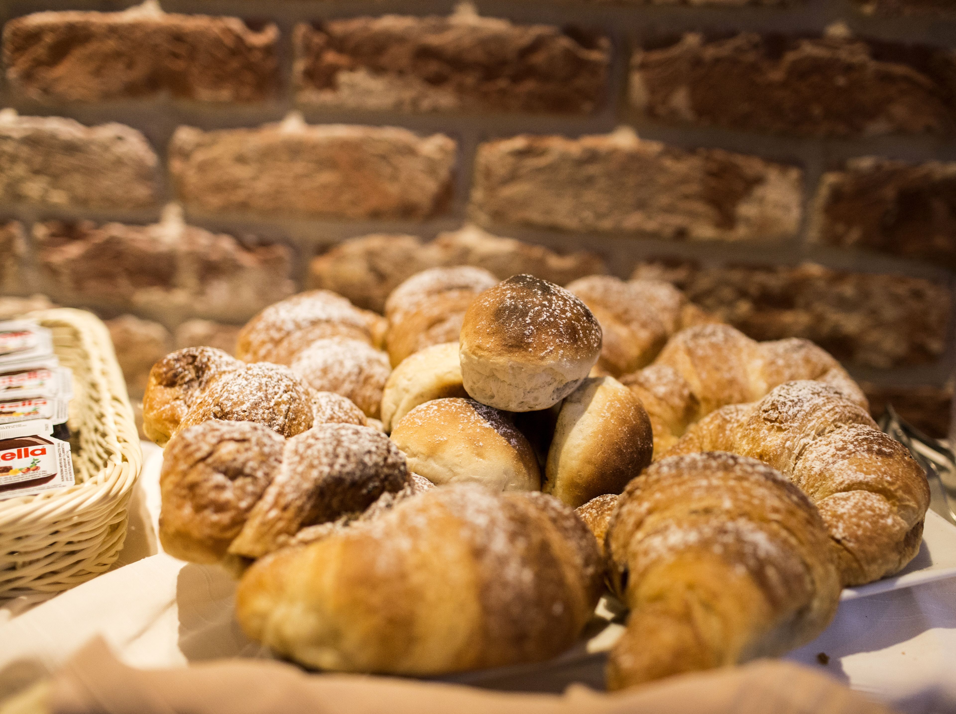A variety of pastries and bread displayed on a table with a brick wall background.