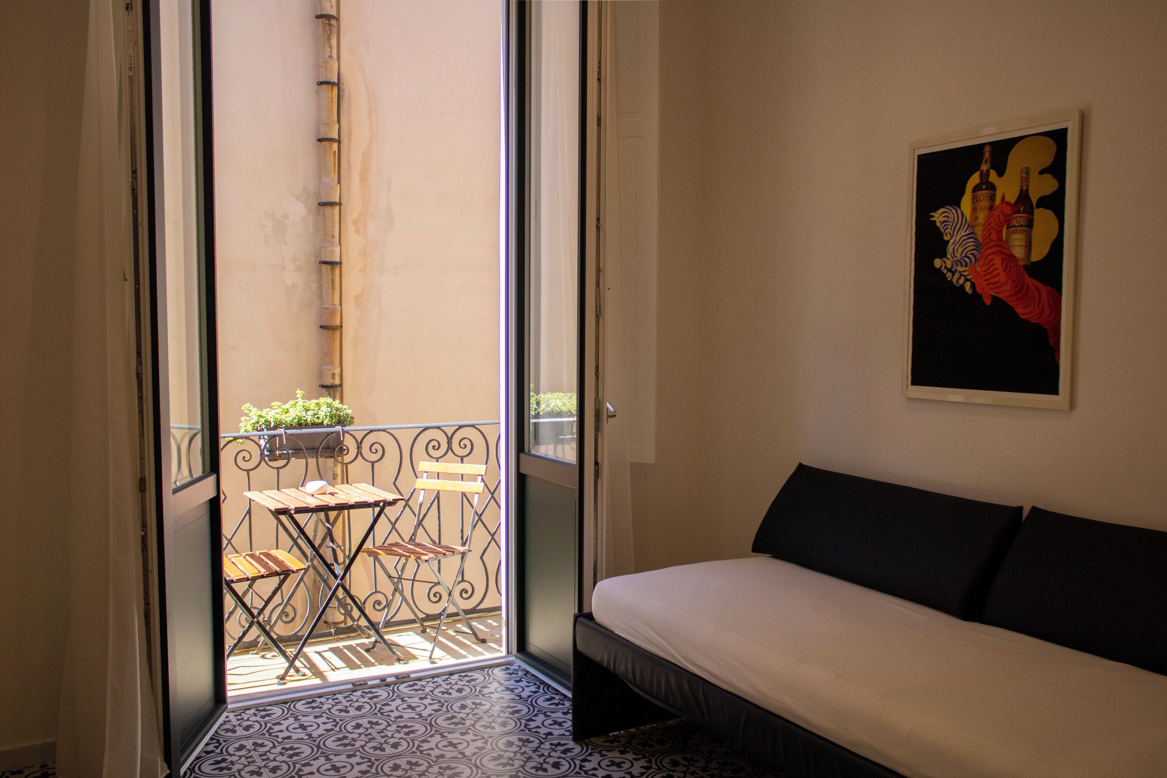 A room with a bed, a painting, and a balcony with a table and chairs.