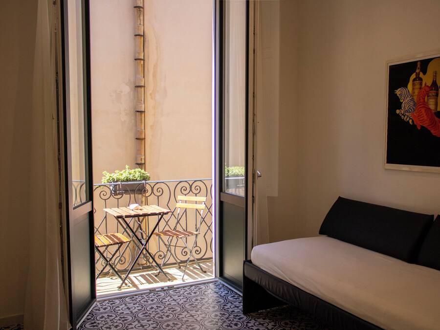 A room with a bed, a painting, and a balcony with a table and chairs.