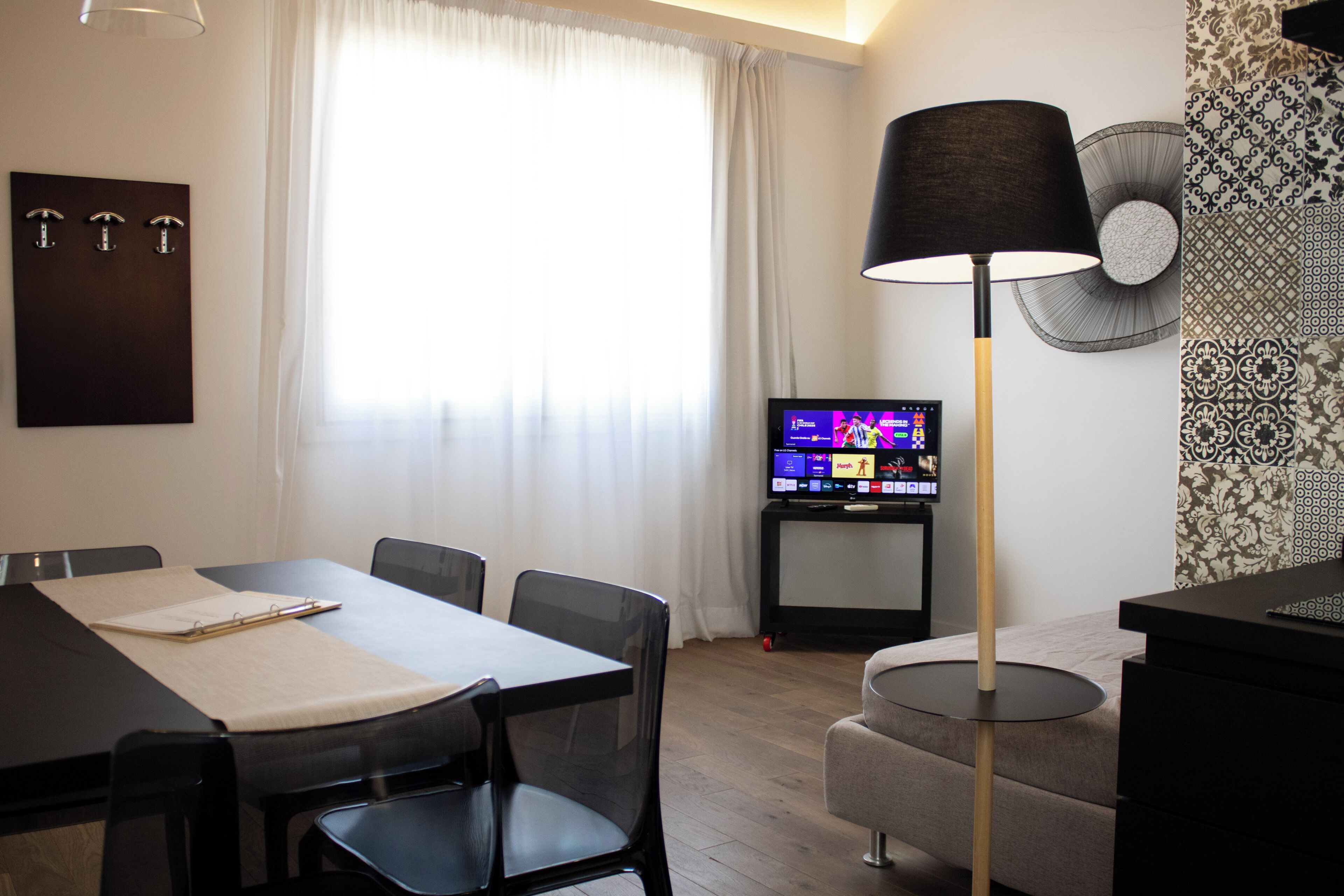 A modern living room with a dining table, chairs, a TV, and a lamp.