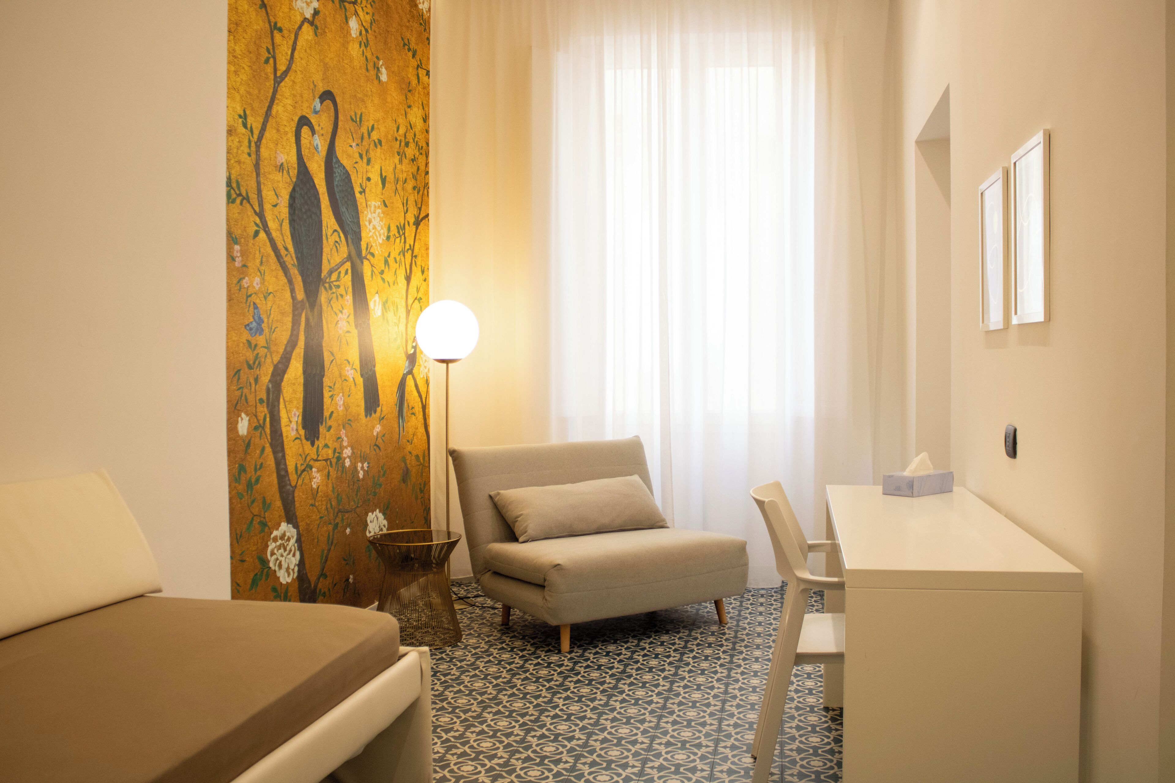 Una habitación de hotel con una cama, un escritorio, una silla, una lámpara y un cuadro en la pared.