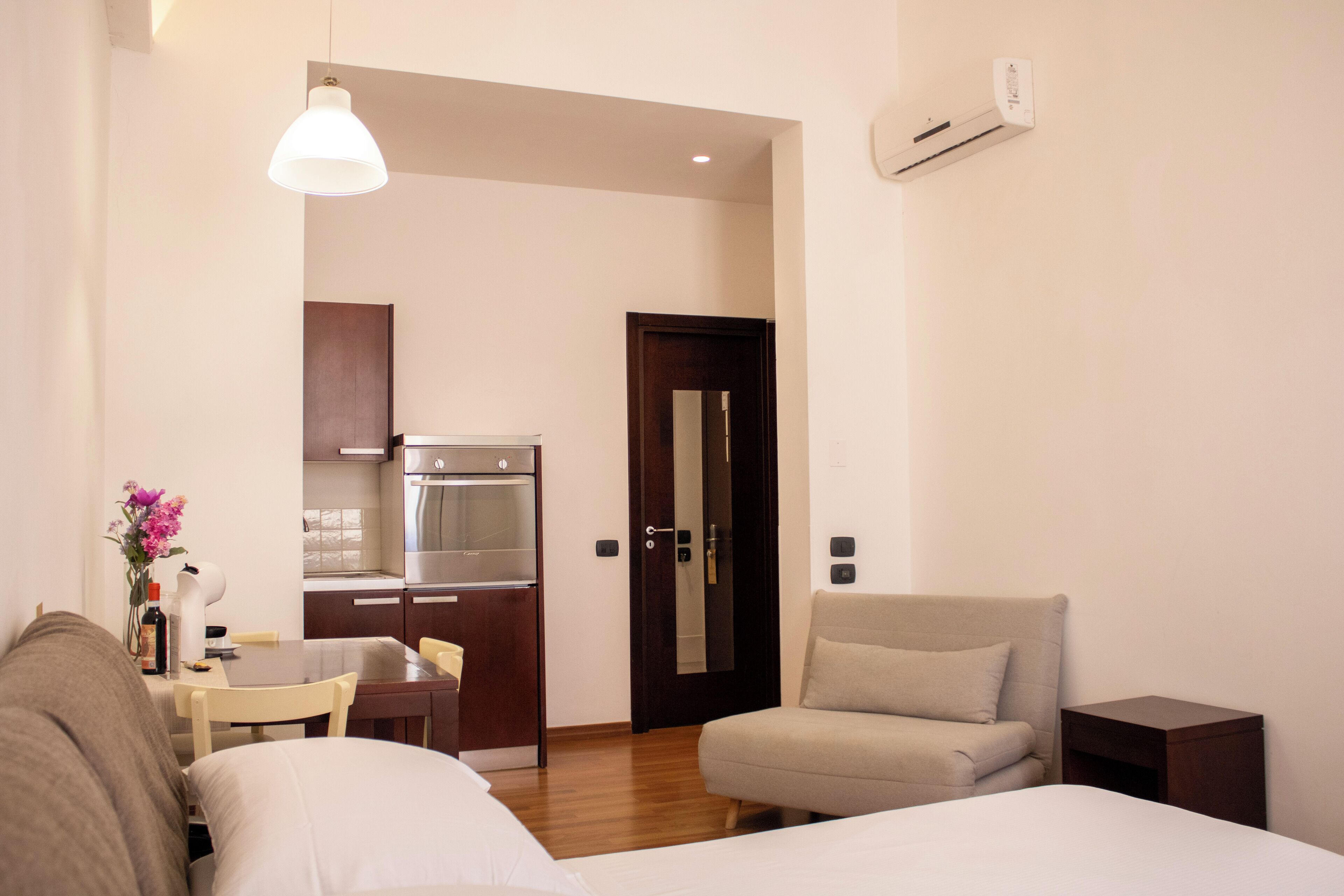 A hotel room with a bed, a sofa, a dining table, and a kitchenette.