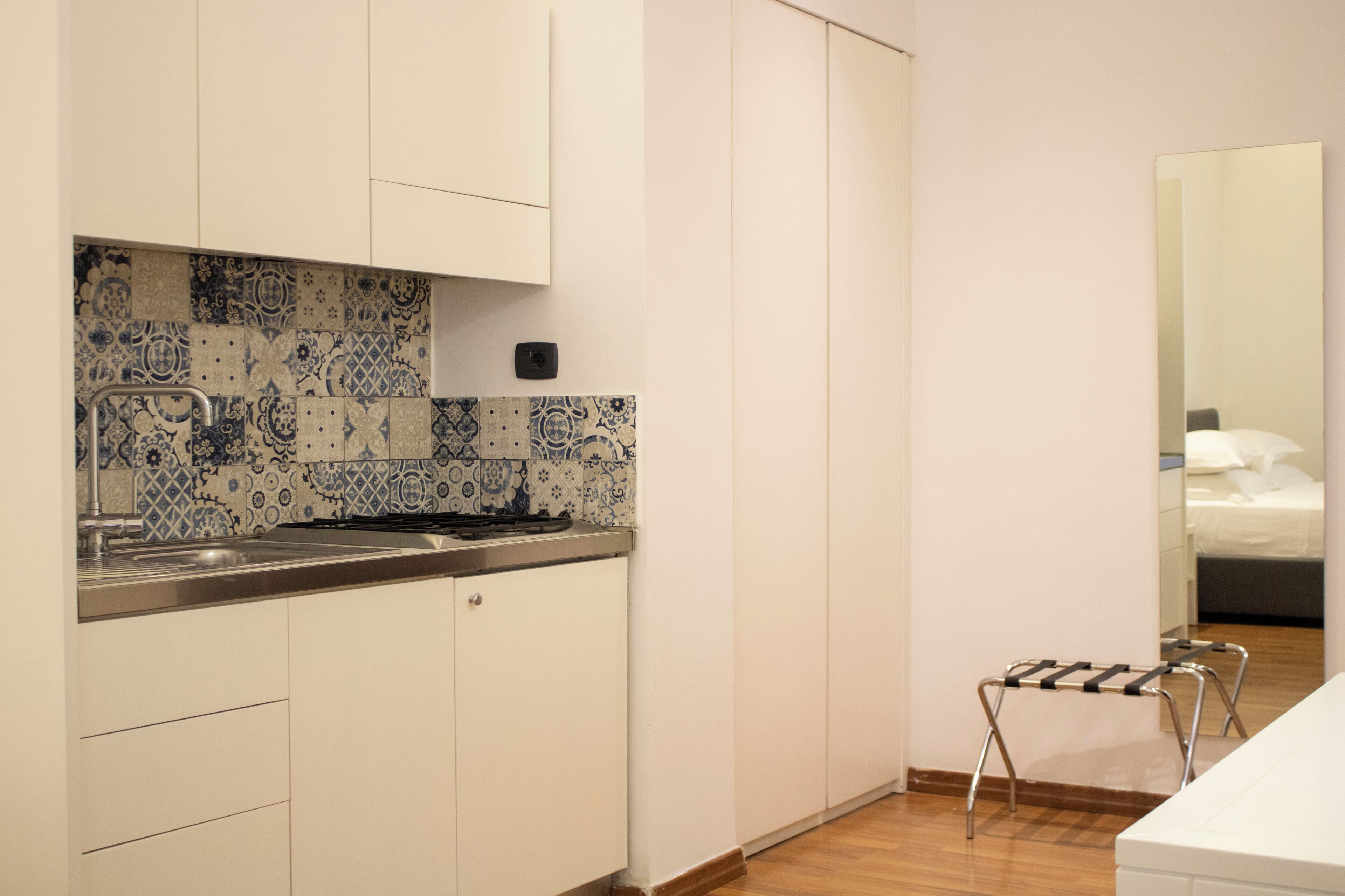 A compact kitchen with white cabinets, a tiled backsplash, and a small stool.