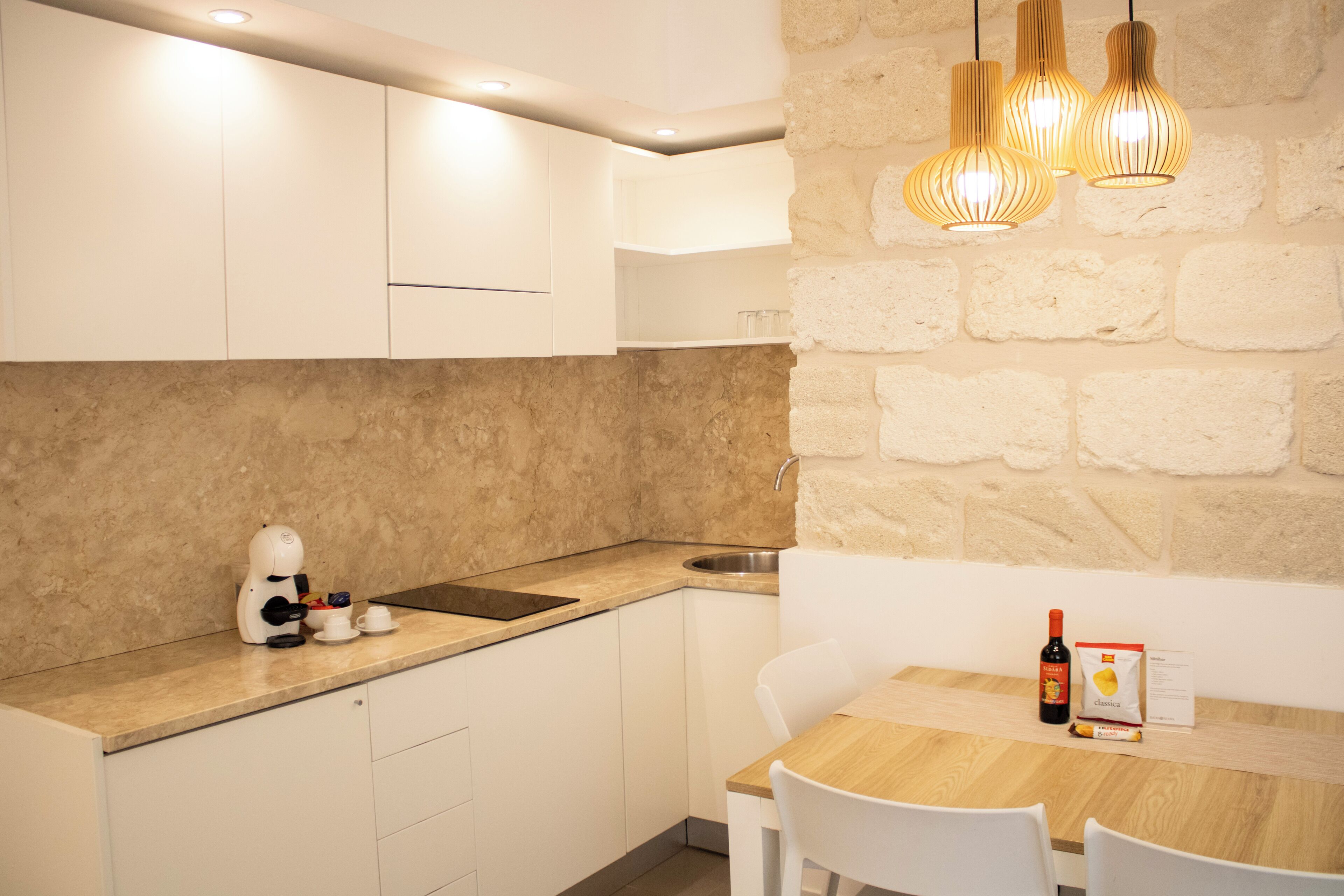 A modern kitchen with white cabinetry, a stone accent wall, and a dining area with a wooden table and white chairs.