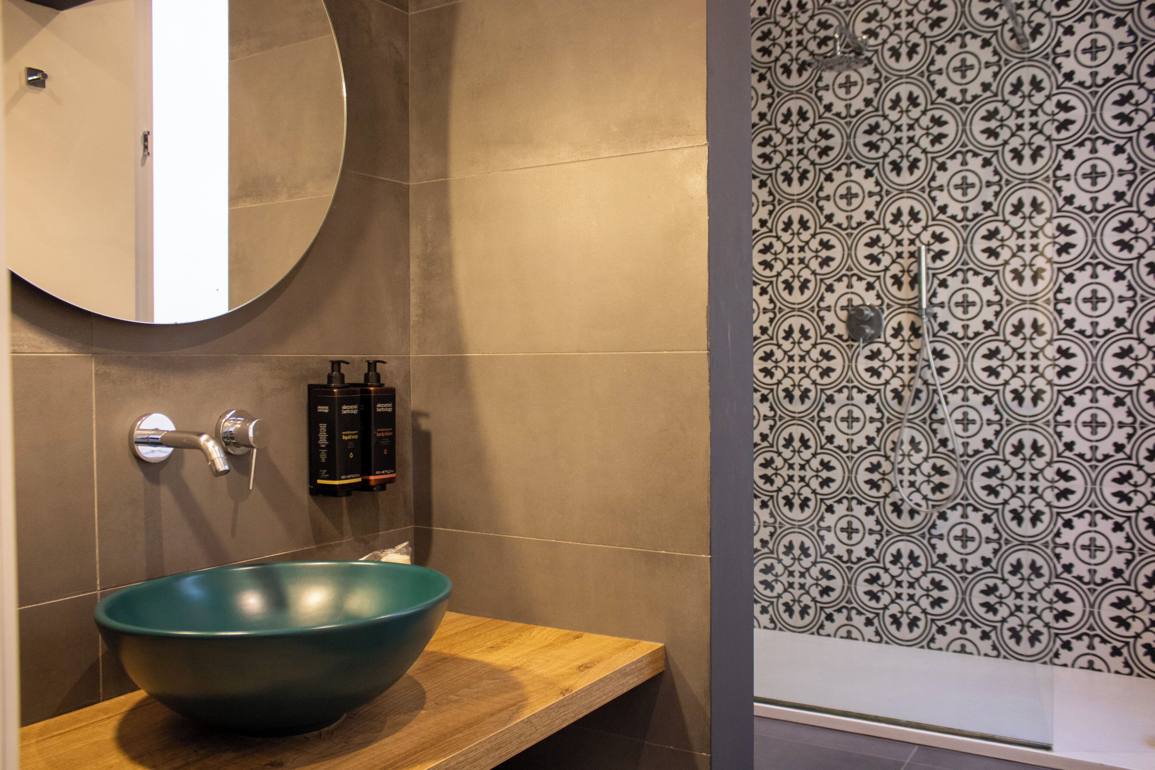 A bathroom with a round mirror, a teal bowl sink, and patterned tile walls.