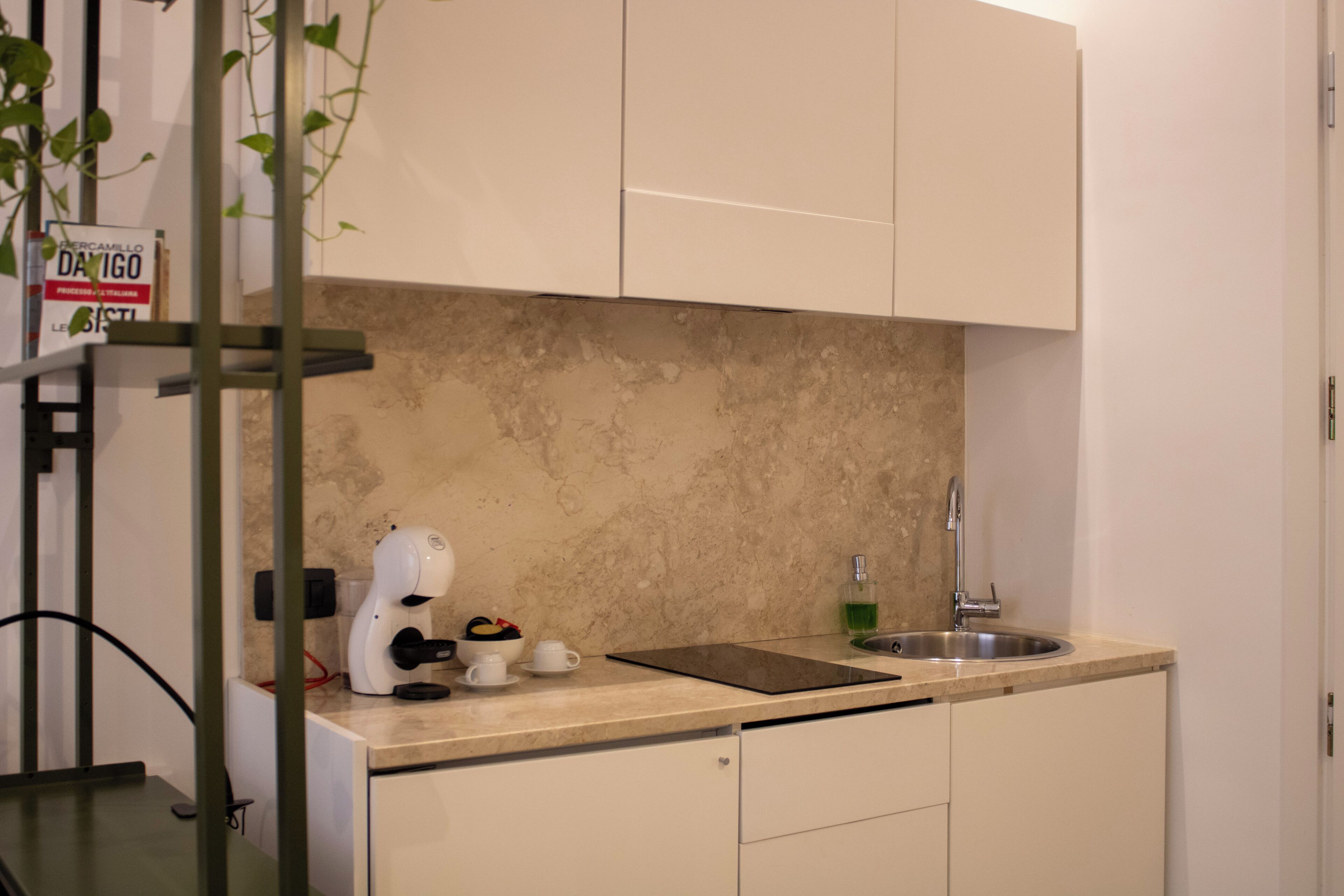 A kitchen with a marble backsplash, a coffee machine, a sink, and a sign on the wall.