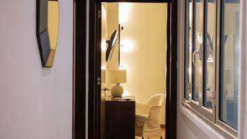 A hallway leading to a room with a desk, chair, lamp, and a large window.