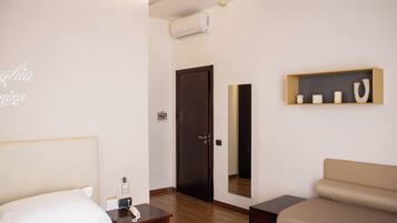 A hotel room with a bed, bedside table, a small desk, a sofa, a mirror, and a shelf with decorative items.