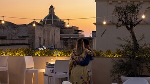 A couple embracing on a terrace with string lights, overlooking a historic building and a tree. - BADIA NUOVA Apart Hotel (Trapani)
